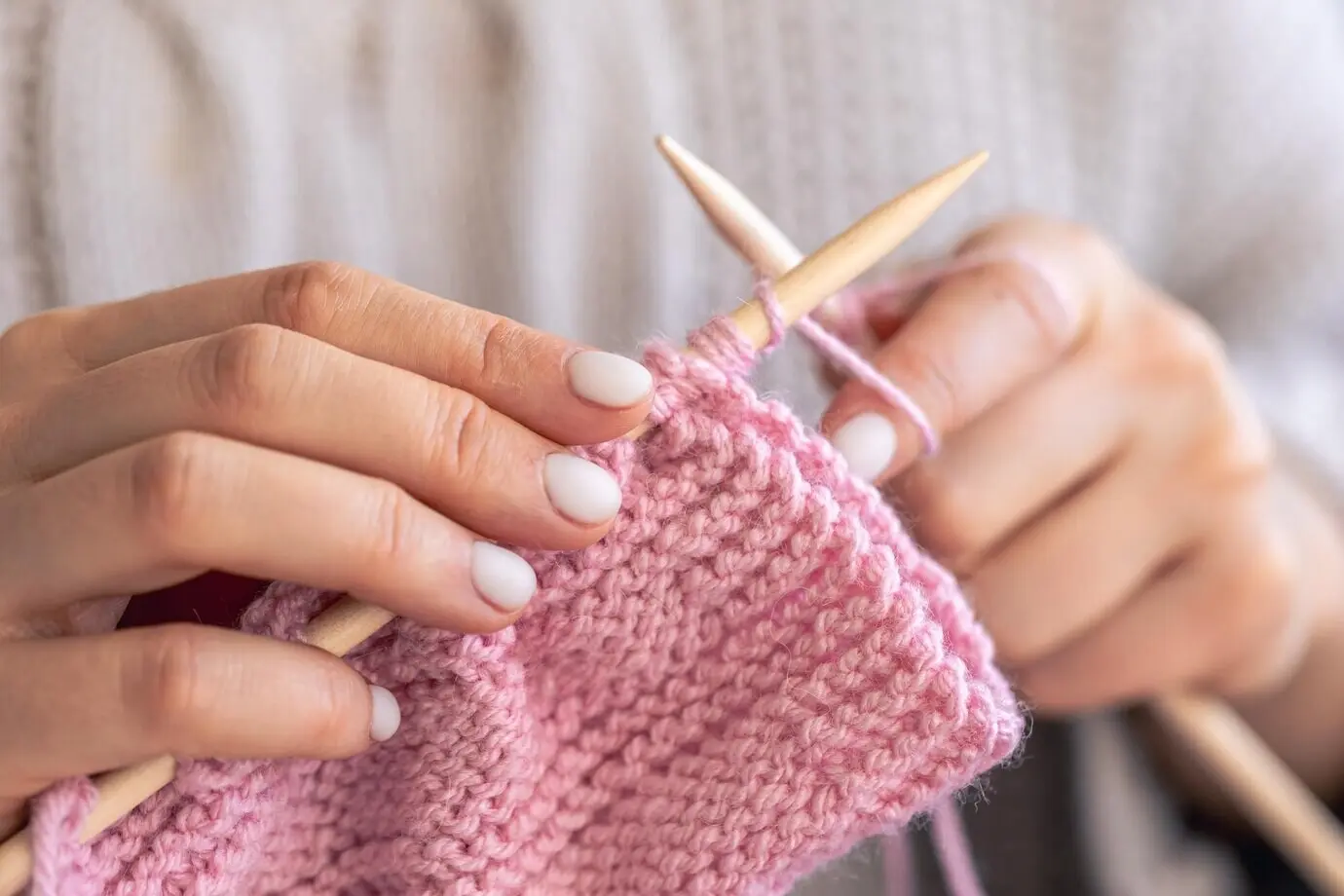Nahaufnahme von Händen beim Stricken mit Rundstricknadeln.