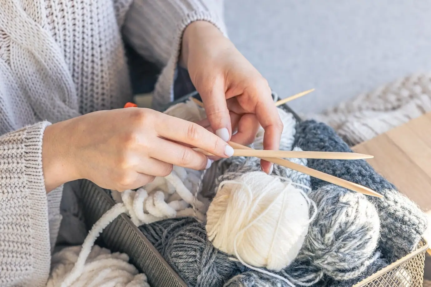 Hölzerne Stricknadeln und ein Garnknäuel in weiblichen Händen